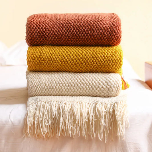 Stack of three knitted blankets in brown, yellow, and beige on a white surface.