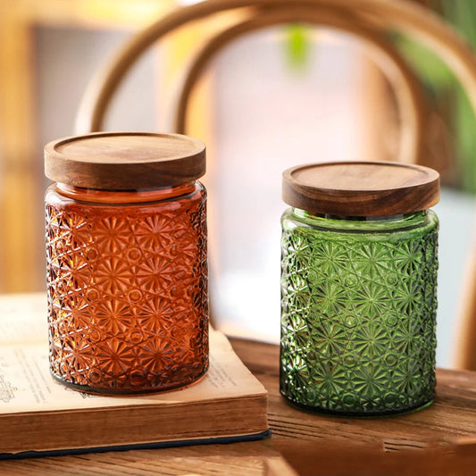 Two textured glass jars with wooden lids on a wooden surface.