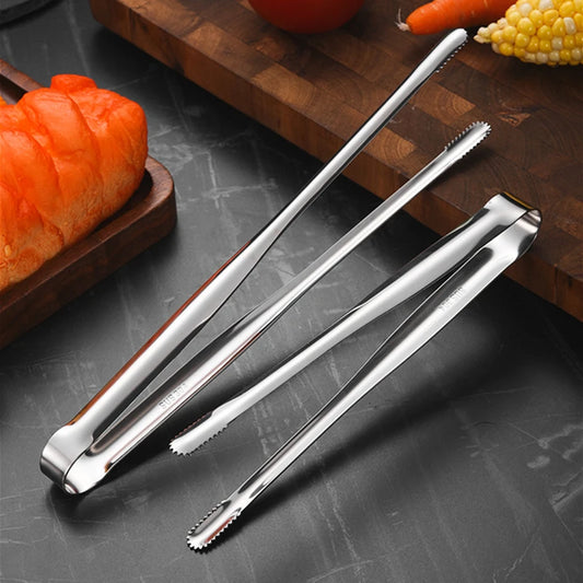 Metal tongs on a dark surface with vegetables in the background