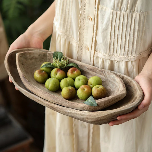 Person holding a wooden bowl with green fruits and vegetables.