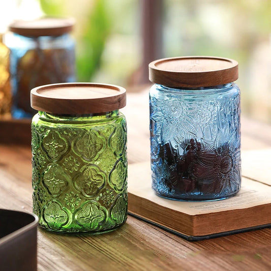 Two glass jars with wooden lids, one green and one blue, on a wooden surface.