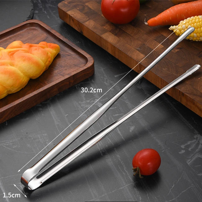 Metal tongs on a dark surface with vegetables and a pastry.