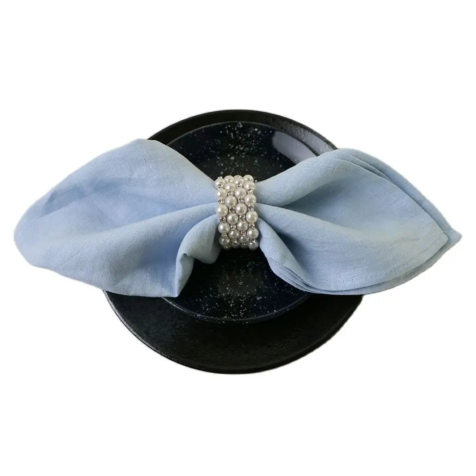 Napkin ring with a pearl detail on a black plate with a light blue napkin.