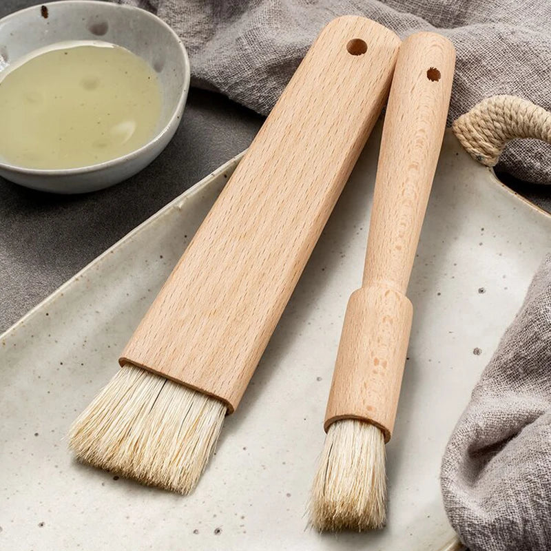 Two wooden brushes with natural bristles on a textured surface with a bowl of liquid and cloth in the background.