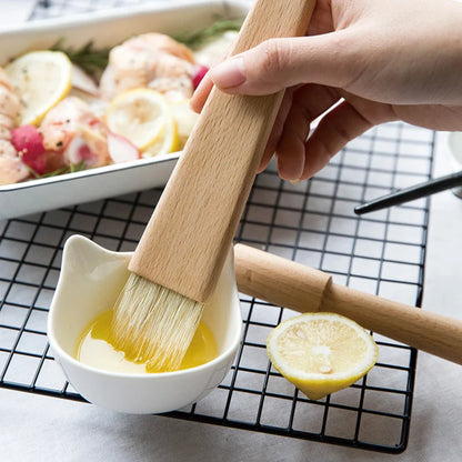 Person using a brush to apply lemon butter sauce on food with a bowl of lemon butter and a lemon slice in the background.
