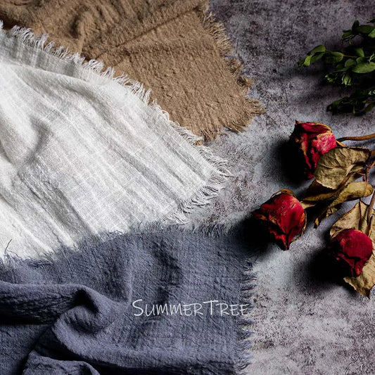 Textured fabric swatches in white, beige, and gray with dried roses on a textured surface.