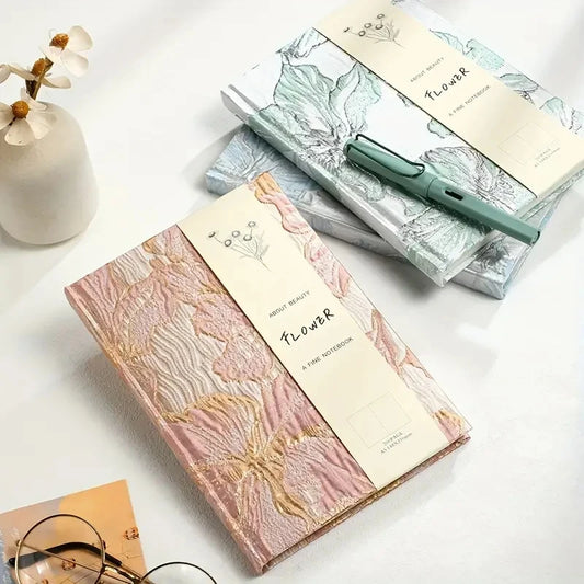 Notebooks with floral design and a pen on a white surface