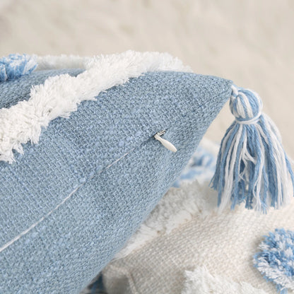 Close-up of a blue textured pillow with white tassels on a neutral background