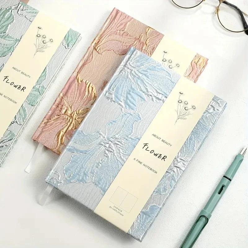 Set of notebooks with floral designs on a white surface with a pen and glasses.