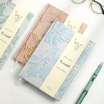 Set of notebooks with floral designs on a white surface with a pen and glasses.