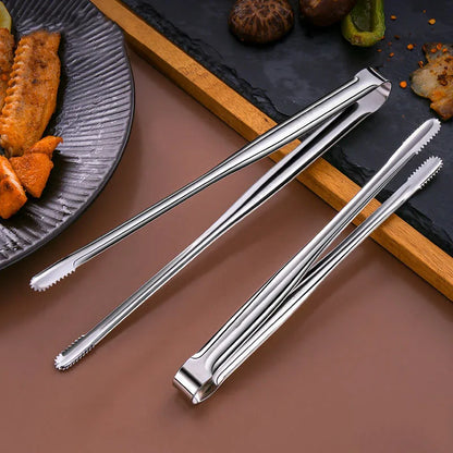 Set of metal tongs on a brown surface with food items in the background