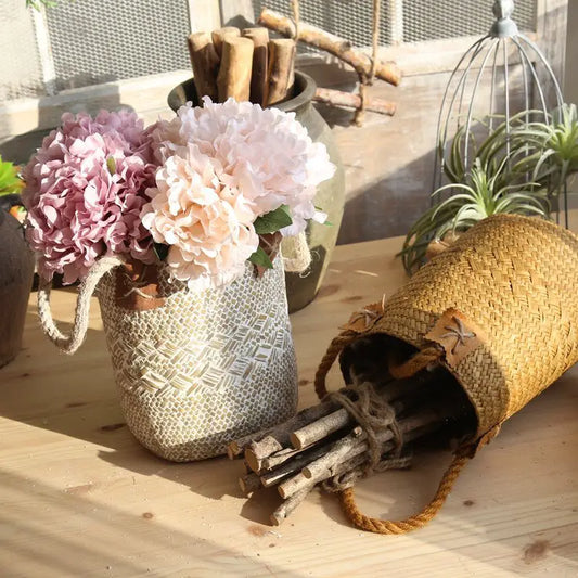 Decorative setting with a textured vase holding flowers, a woven basket, and sticks on a wooden surface.