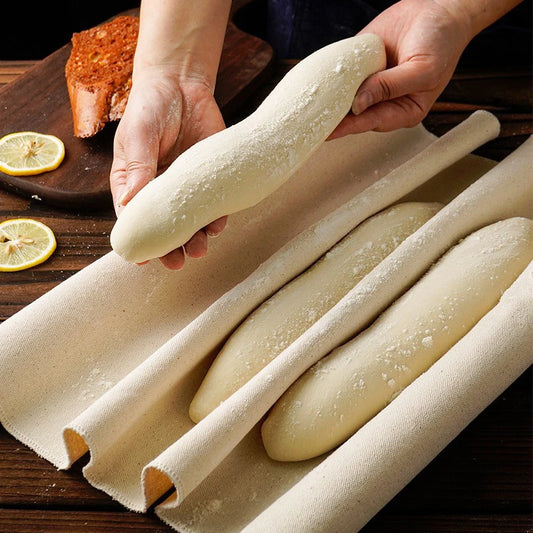 Person handling rolled dough on a wooden surface with lemons and bread in the background