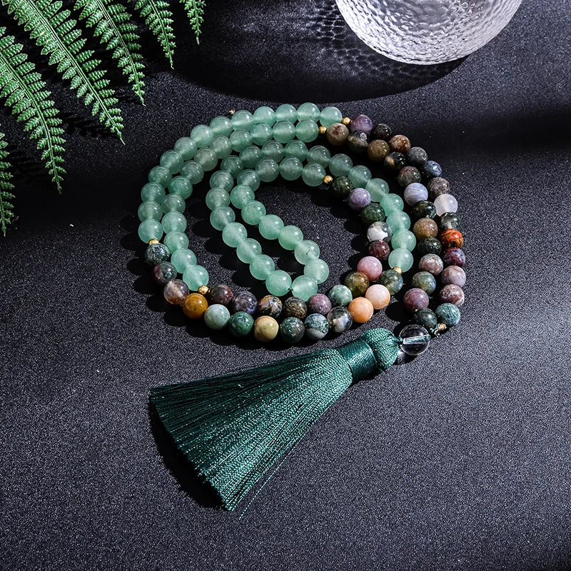 Multicolored beaded necklace with a green tassel on a dark surface with fern leaves.
