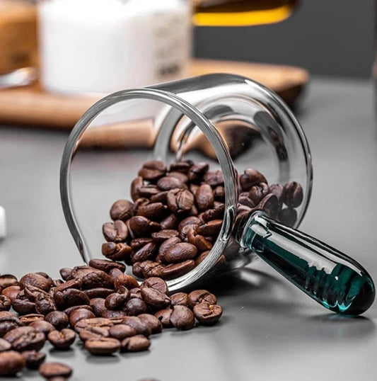 Glass container with coffee beans spilling out on a gray surface