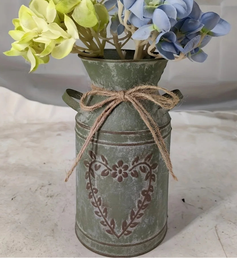 Decorative green metal vase with floral arrangement on a light surface
