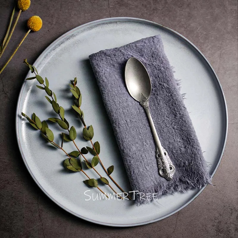 Silver spoon on a purple napkin with green leaves and yellow flowers on a gray plate.