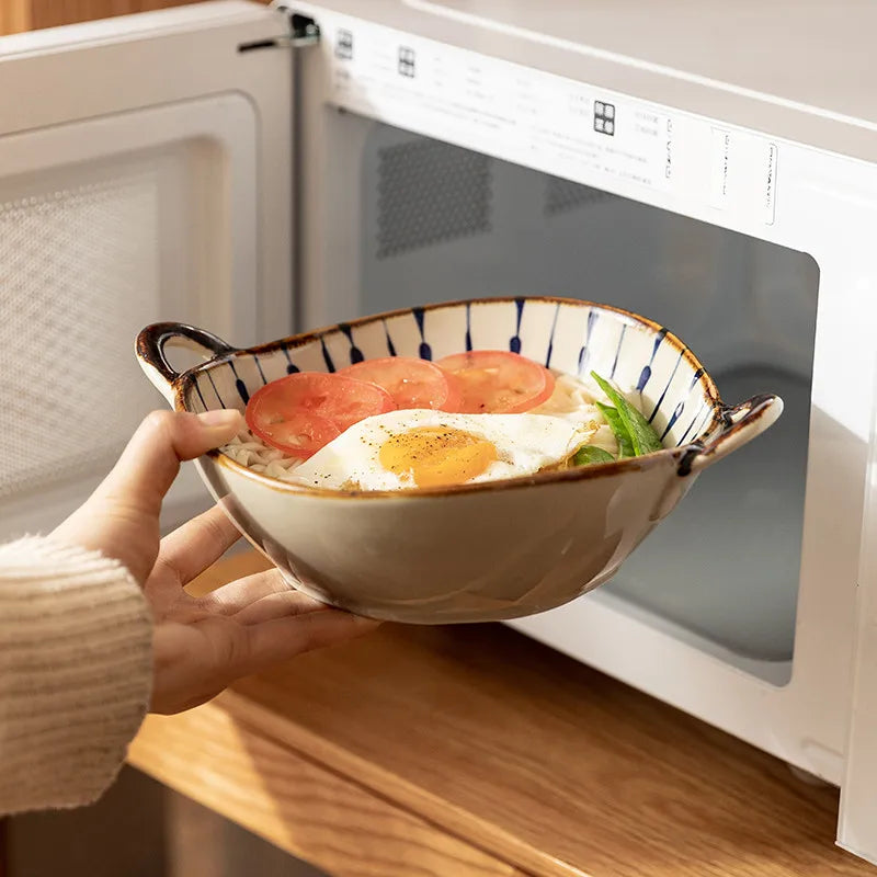 Person holding a bowl of food in front of an open microwave.