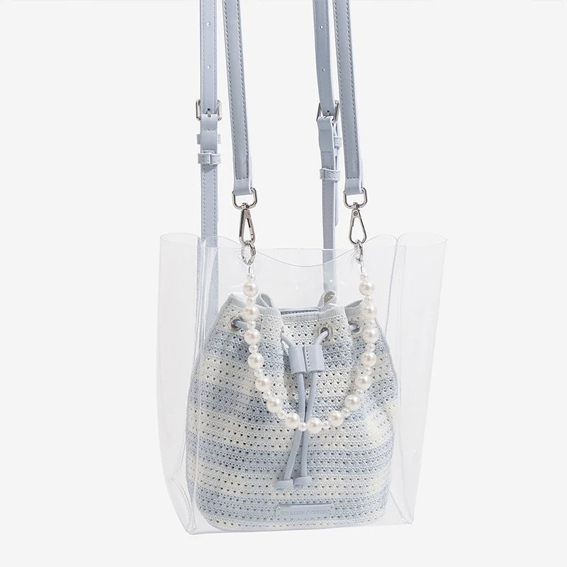 Clear handbag with a textured gray bag inside and pearl necklace on a white background