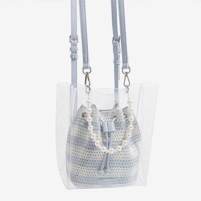 Clear handbag with a textured gray bag inside and pearl necklace on a white background
