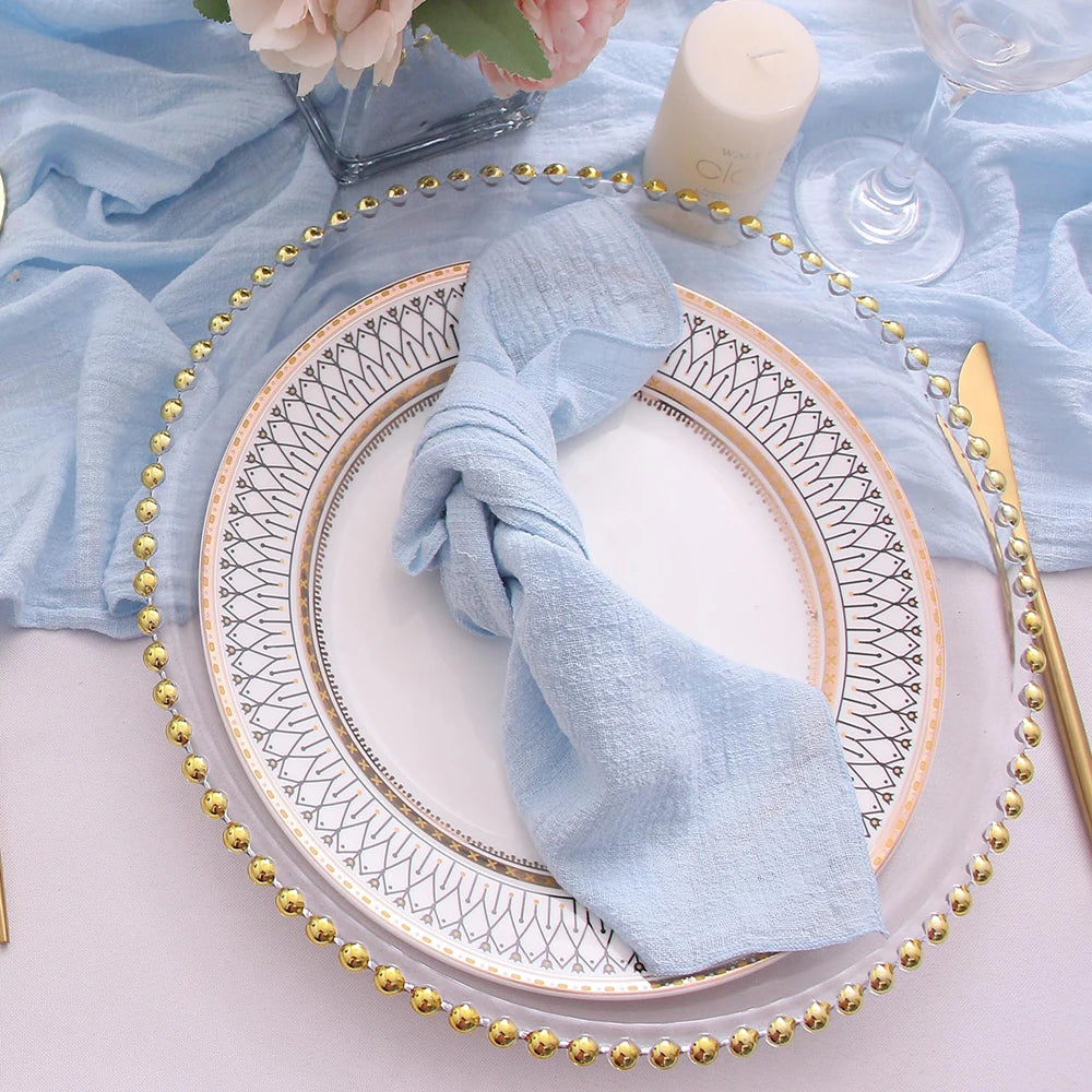 Decorative table setting with a plate, gold rim, and blue napkin on a light blue fabric background.