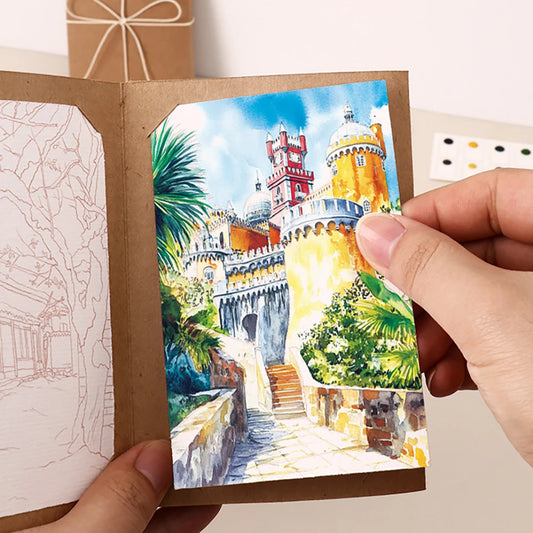 Hand holding a small painting of a castle with greenery