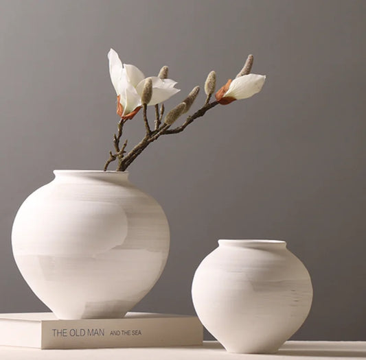 Two white ceramic vases with a branch of flowers on a gray background