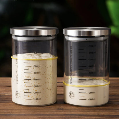 Two glass fermentation tanks with metal lids on a wooden surface.