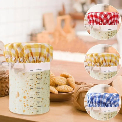 Measuring cup with checkered coverings on a kitchen counter with cookies and a basket.