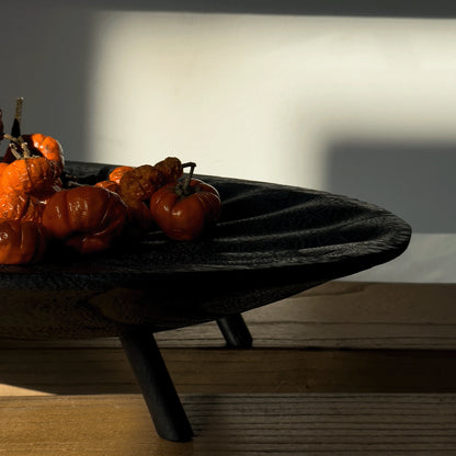 Decorative black bowl with orange and red fruits on a wooden surface