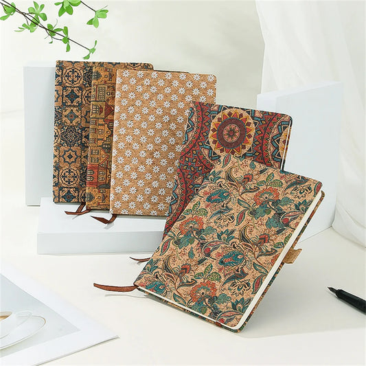 Three patterned notebooks on a white surface with a plant in the background