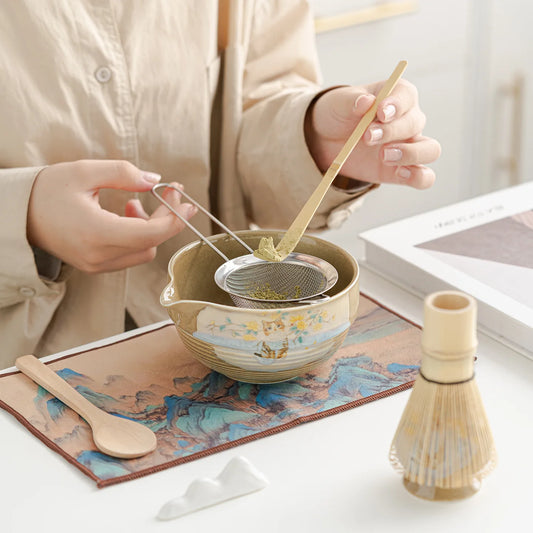 Person using tea-making tools on a table with a decorative mat