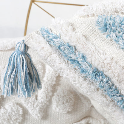 Close-up of a textured white blanket with blue tassels and fringe.