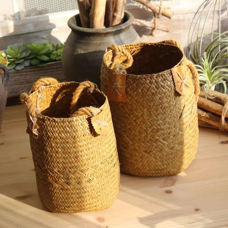 Two woven baskets on a wooden surface with plants in the background
