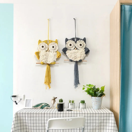 Two owl-shaped wall decorations hanging on a white wall above a table with plants.