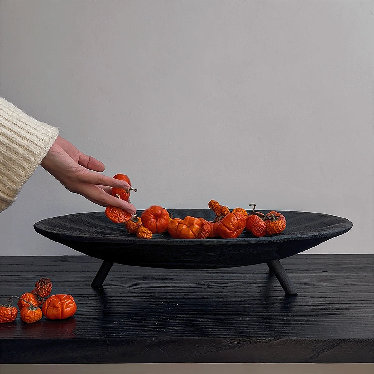 Person arranging roasted peppers on a black decorative plate with a plain background