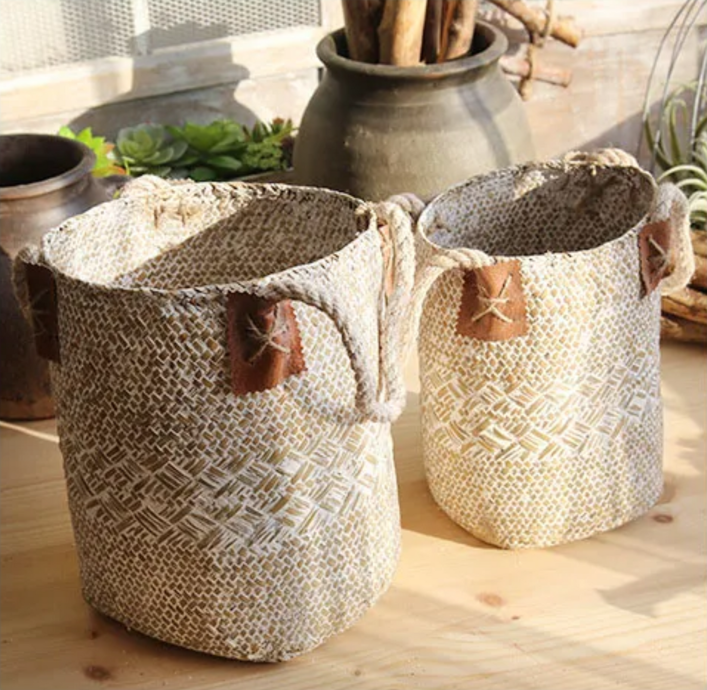 Two woven baskets with leather handles on a wooden surface.