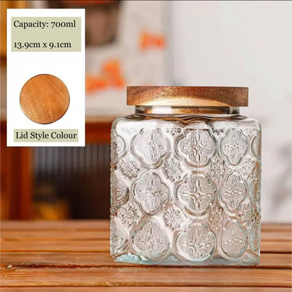 Decorative glass jar with embossed design and wooden lid on a wooden surface.