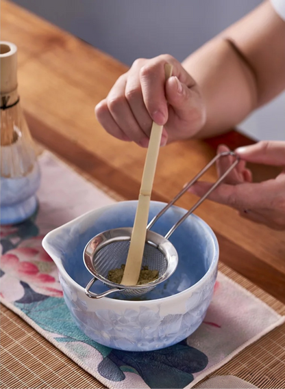 Person using a tea strainer in a blue ceramic teacup on a wooden table.