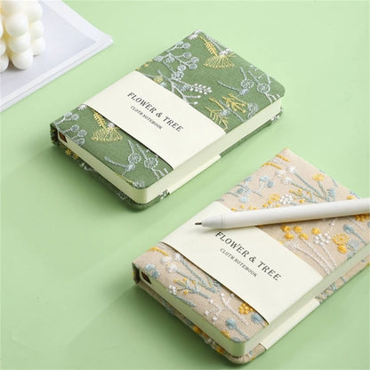Two floral notebooks with a pen on a green background