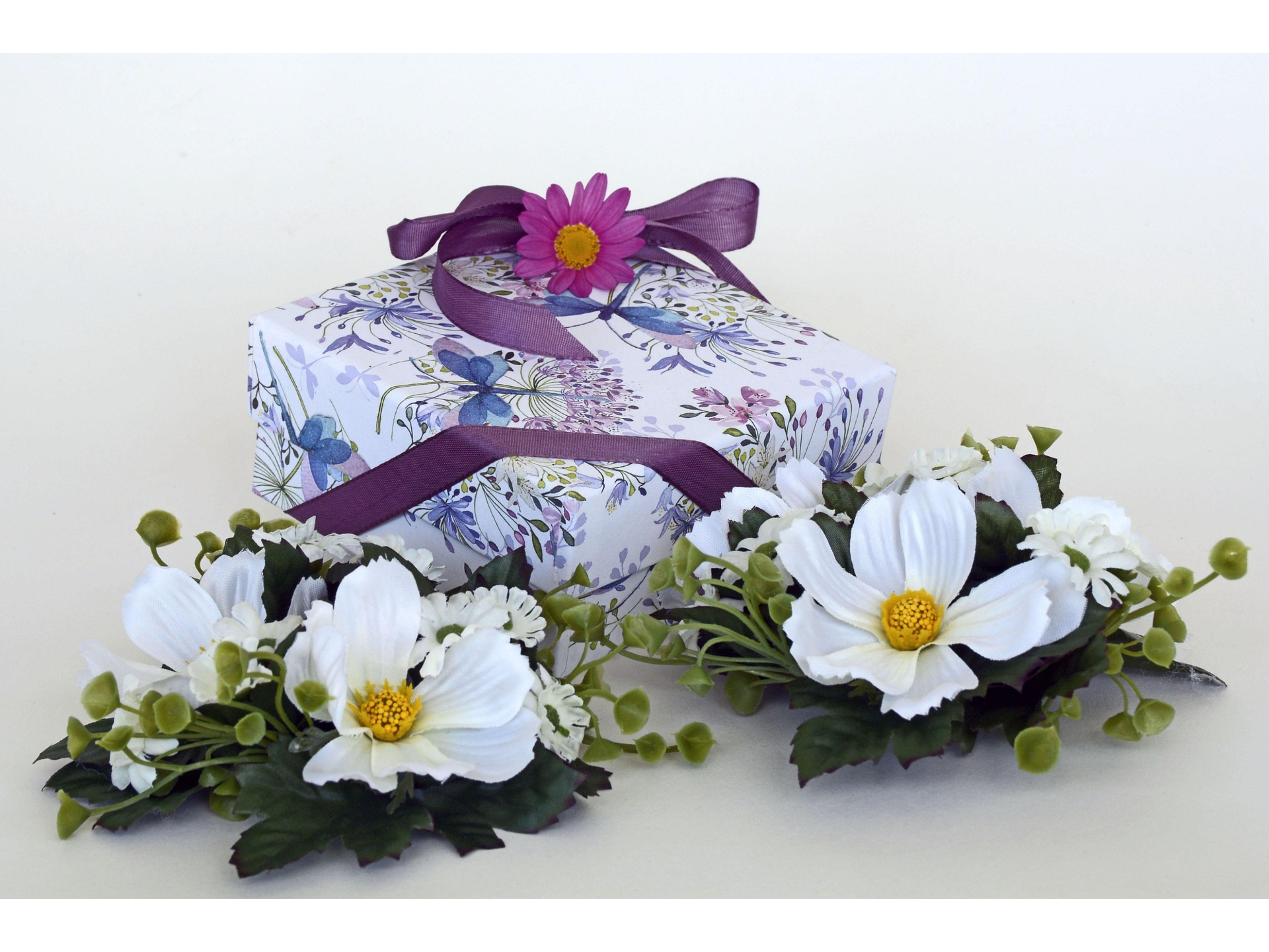 Decorative box with floral design and ribbons, accompanied by white flowers on a white background