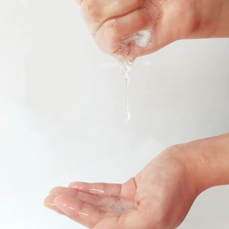 Hand pouring clear liquid from a container onto another hand against a white background
