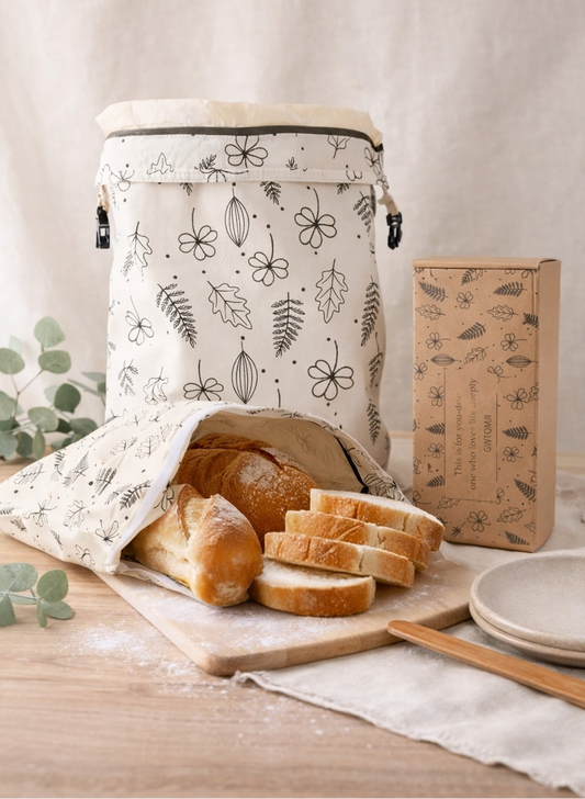 Fabric bread bag with floral patterns on a table with sliced bread and a box.