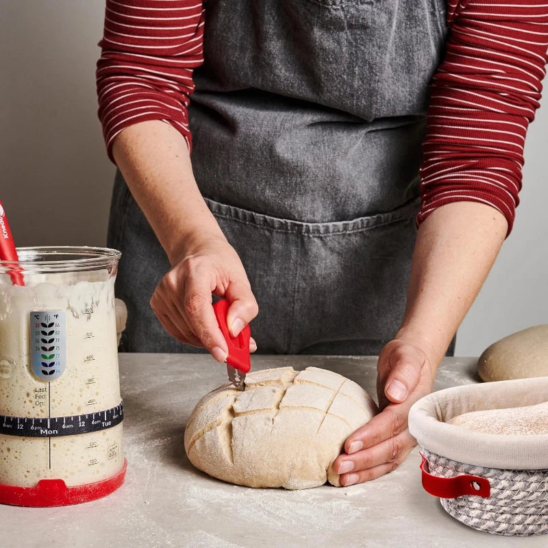 Person cutting a loaf of bread with a knife on a countertop, wearing a gray apron.