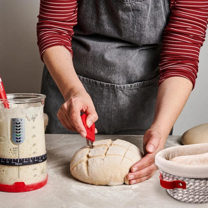 Person cutting a loaf of bread with a knife on a countertop, wearing a gray apron.