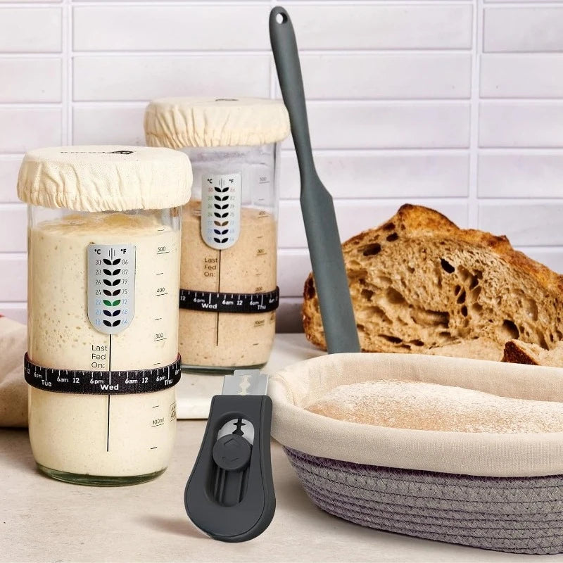 Bread-making tools including jars with measuring devices and a spatula on a kitchen counter.