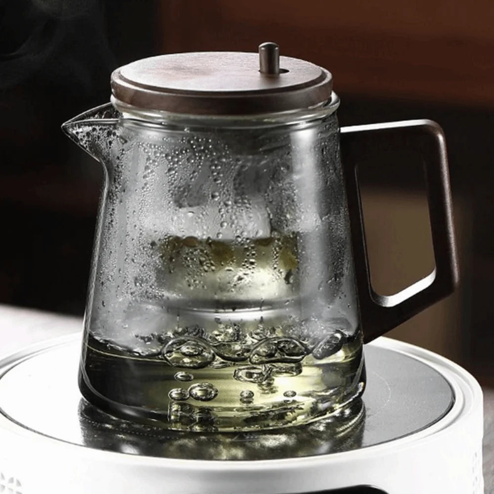 Clear glass teapot with wooden lid on a white surface
