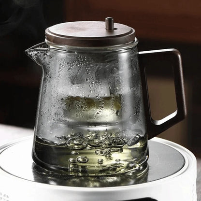 Clear glass teapot with wooden lid on a white surface