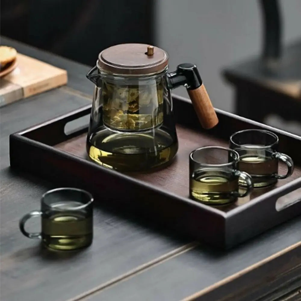 Glass teapot and cups on a wooden tray with a blurred background