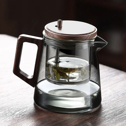 Clear glass teapot with wooden handle and lid on a wooden surface